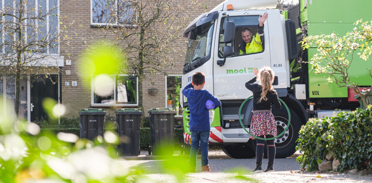 Foto van ROVA inzamelwagen waarbij chauffeur zwaait naar kinderen die terugzwaaien
